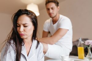 Upset girl with straight brown hair posing at home with sad man on background. Indoor portrait of unhappy married couple wear pajamas in morning..